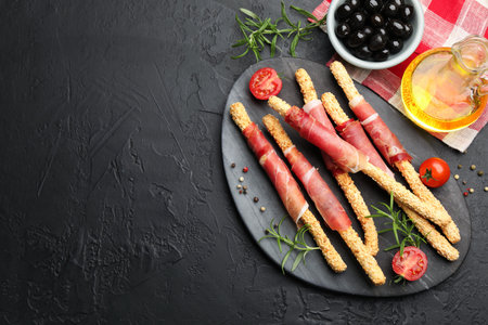 Delicious grissini sticks with sesame seeds, prosciutto, peppercorns, rosemary and tomatoes on dark...