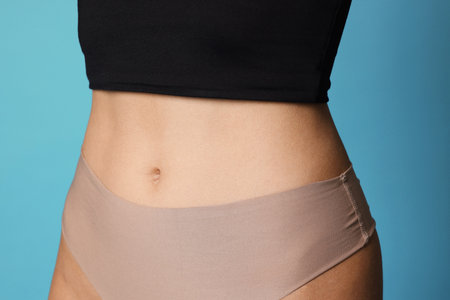 Young woman with flat belly on light blue background, closeup