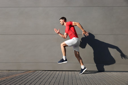 Man in sportswear running near building outdoors, space for text