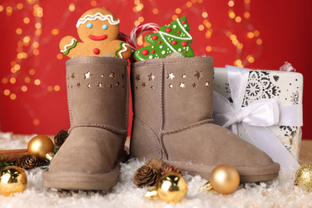 Saint Nicholas day. Boots filled with treats, festive decor and gift box on table against red...
