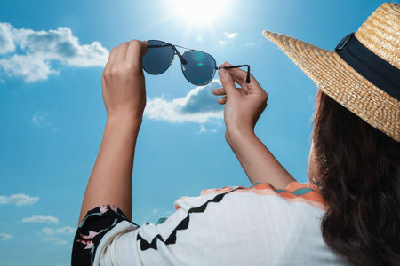 Woman holding funny sunglasses against blue sky on sunny day, low angle view
