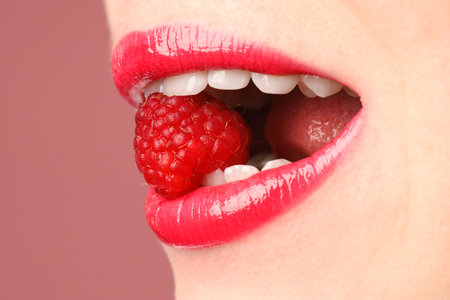 Woman with beautiful lips makeup and raspberry on dusty pink background, closeup. Space for textの写真素材