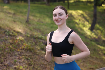 Smiling woman in sportswear running in park. Space for text