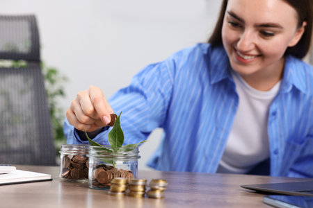 Woman putting coins into glass jar at wooden table indoors, selective focusの写真素材