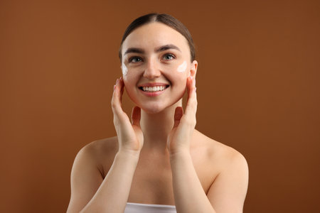 Beautiful woman with cream on her face against brown backgroundの写真素材