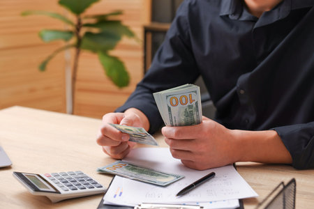 Man counting dollar banknotes at wooden table, closeup