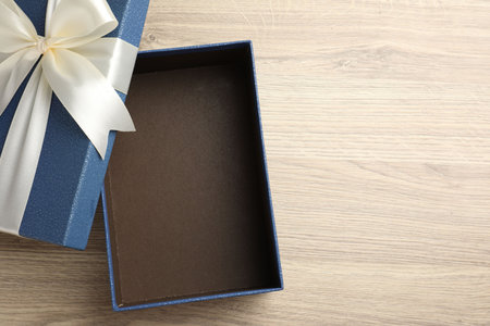 Opened gift box with beautiful lid on light wooden table, top view. Space for text