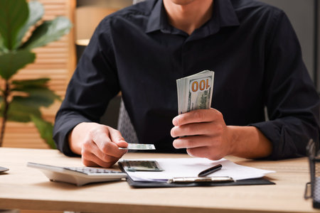 Man counting dollar banknotes at wooden table, closeup