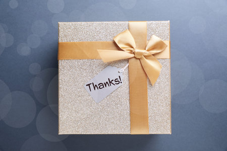 Thanks tag attached to gift box on pale blue background. Bokeh effect