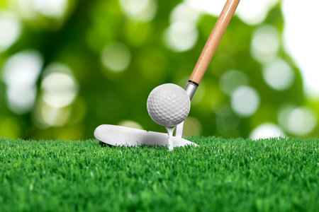 Golf ball, tee, club and green grass against blurred backgroundの写真素材