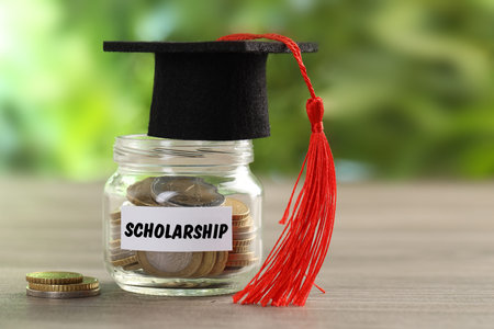 Scholarship. Jar with coins and graduate hat on wooden tableの写真素材