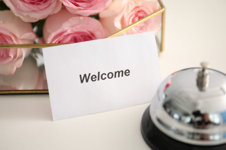 Card with Welcome word, desk bell and roses on white table, closeupの写真素材