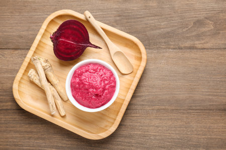 Tasty horseradish sauce with beetroot, spoon, roots and vegetable on wooden table, top view. Space for textの写真素材