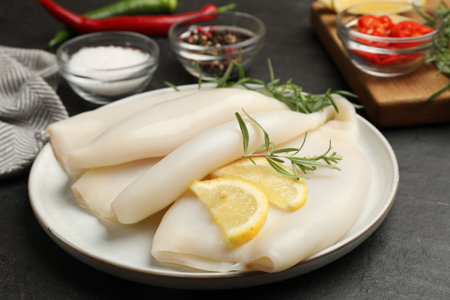 Uncooked squids with lemon slices, rosemary and spices on black table, closeupの写真素材