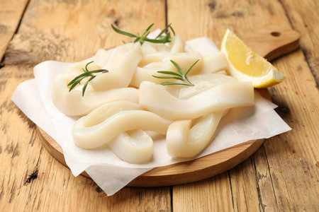 Uncooked squid rings with lemon slice and rosemary on wooden table, closeupの写真素材