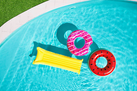Inflatable rings and mattress floating in swimming pool surrounded, top view