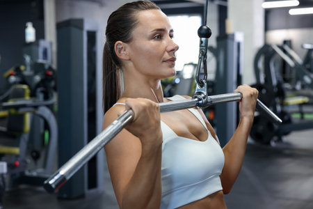 Athletic woman training on lat pulldown machine in gym
