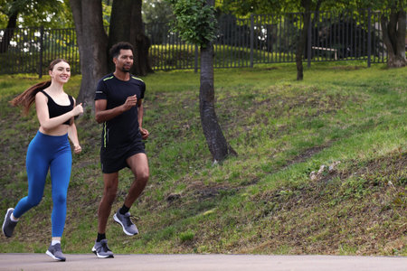 Couple in sportswear running in park, low angle view. Space for text
