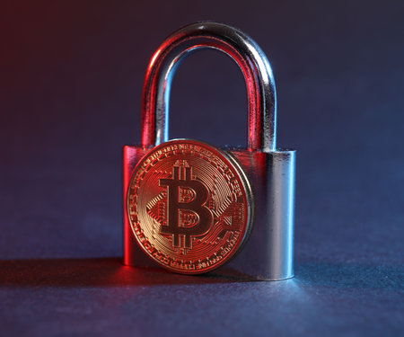 Bitcoin and padlock on blue background in red light, closeup