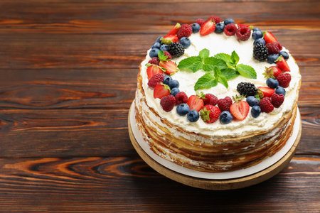 Delicious crepe cake with fresh berries on wooden table, closeup. Space for text