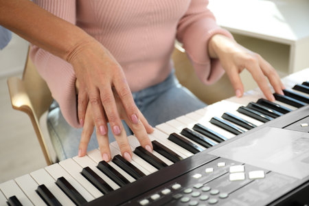 Tutor teaching woman to play piano indoors, closeup