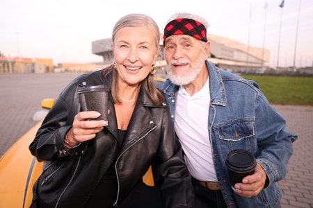 Stylish senior couple with takeaway coffee near modern cabriolet outdoorsの写真素材