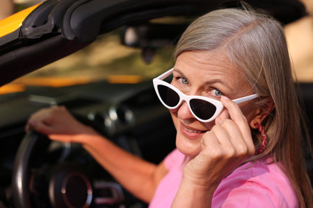Stylish senior woman in sunglasses driving modern cabriolet outdoors