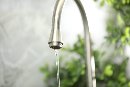 Water saving concept. Stream of water flowing from tap indoors, closeup