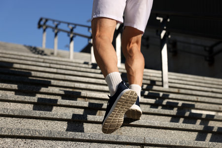 Man in sportswear running up on stairs outdoors, low angle view. Space for text