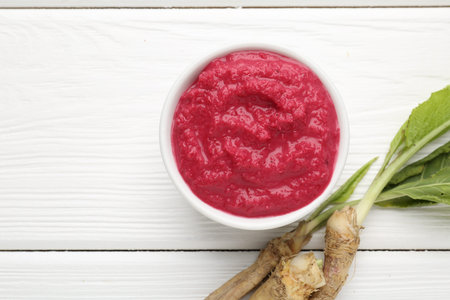 Tasty horseradish sauce with beetroot, vegetable and roots on white wooden table, flat lay. Space...