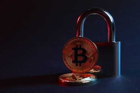 Bitcoins and padlock on blue background in red light, closeup with space for text