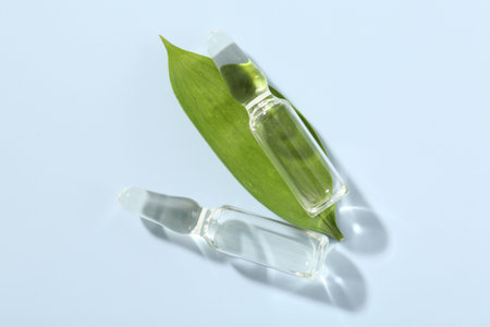 Glass ampoules with cosmetic product and green leaf on light blue background, flat lay