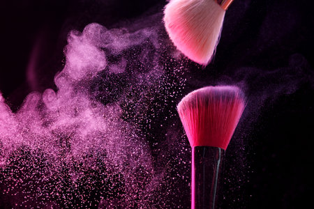Makeup brushes with pink eye shadow on black background, closeup.