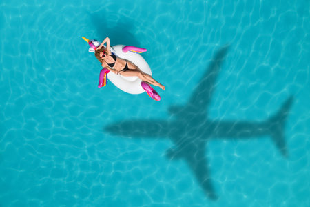 Young happy woman with inflatable ring in swimming pool, above view. Flying airplane casting shadow on waterの写真素材