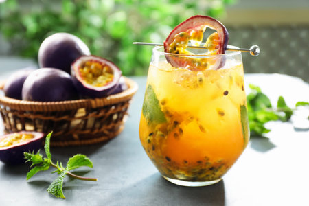 Tasty passion fruit drink in glass, fresh fruits and mint on gray table, closeup