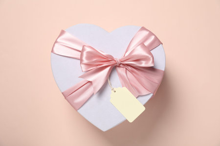 Heart-shaped gift box with blank tag on pale pink background, top view