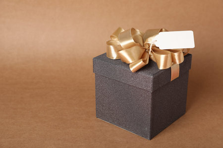 Gift box with blank tag on brown background, closeup. Space for text