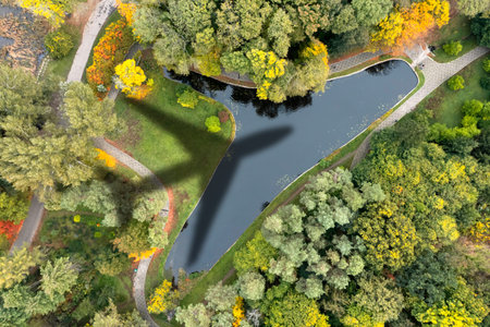 Flying airplane casting shadow on beautiful park with artificial pond, top view
