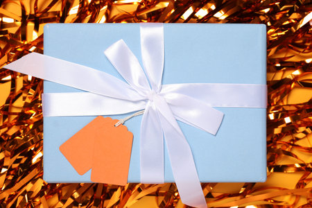 Gift box with blank tags and streamers on orange background, flat lay