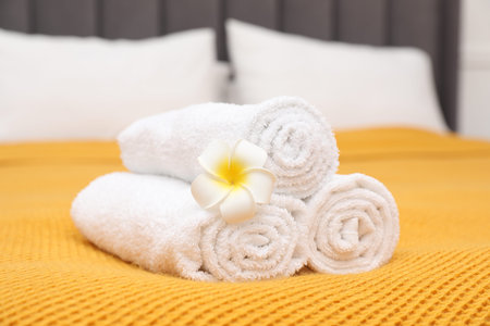 Rolled white terry towels and plumeria flower on bed indoors, closeupの写真素材