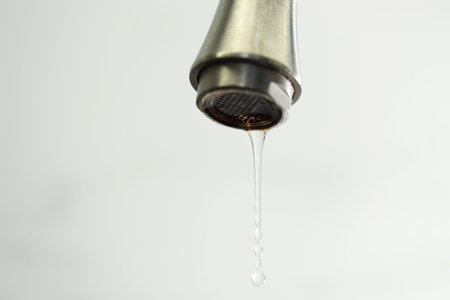 Water saving concept. Water dripping from tap on light background, closeup