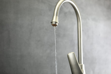 Save water concept. Stream of water flowing from tap against gray background, closeup