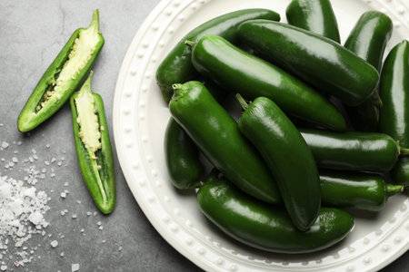 Ripe green jalapeno peppers and salt on gray table, flat lay