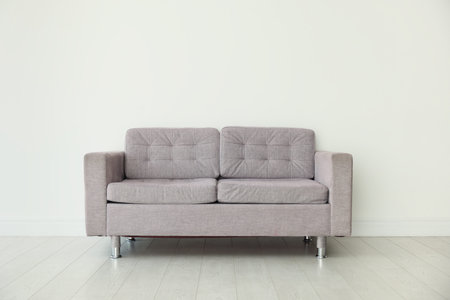 Comfortable gray sofa near white wall in room