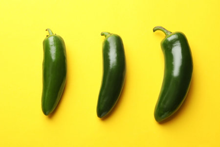 Green jalapeno peppers on yellow background, flat lay