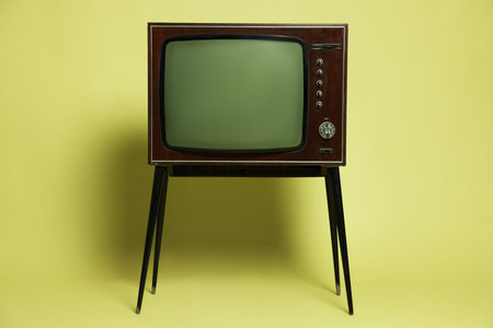 Retro TV set on stand against olive background.