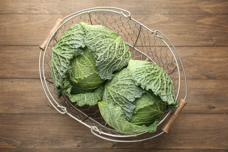 Fresh Savoy cabbages in metal basket on wooden table, top view