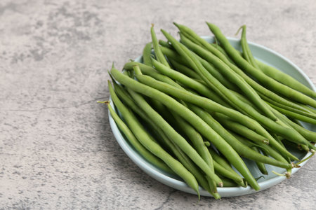 Fresh green bean pods on gray textured table, closeup. Space for text