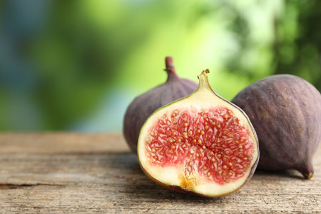 Fresh ripe figs on wooden table outdoors, closeup. Space for text