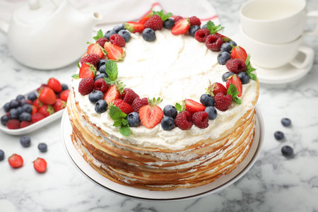 Delicious crepe cake with fresh berries on white marble table, closeup